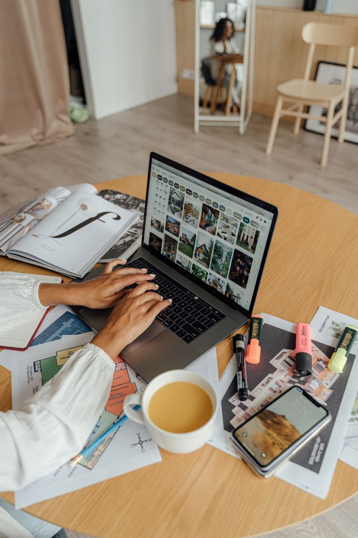 A person working from home with a laptop, coffee, and magazines on a wooden table, showcasing a freelancing lifestyle.