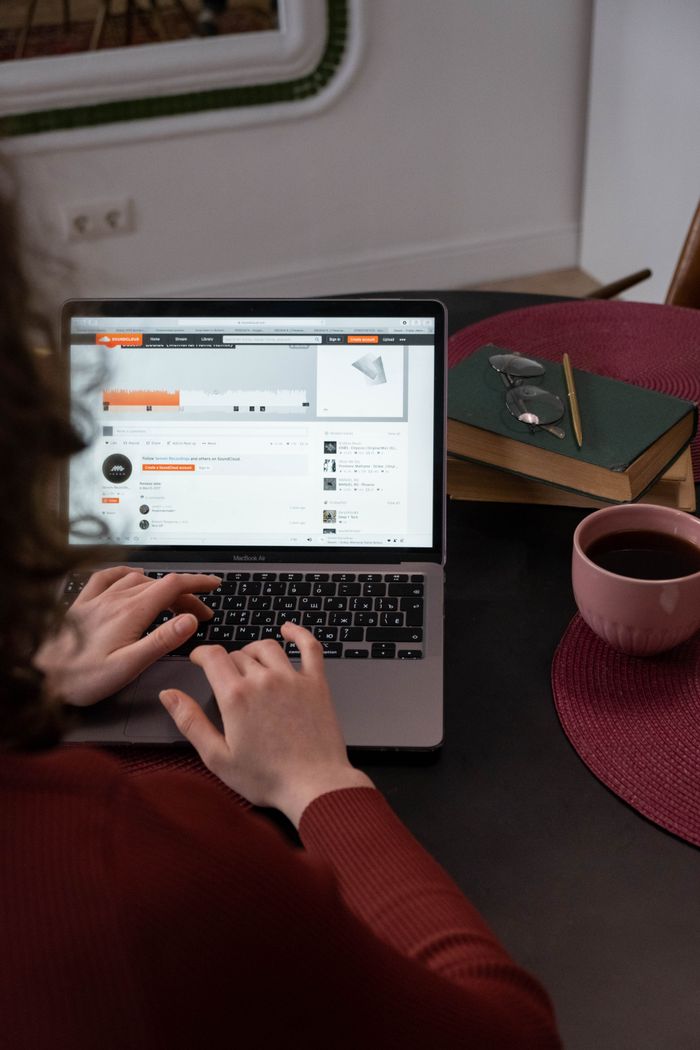 A person works on a laptop indoors, with coffee and books on the table. Ideal for home office concepts.